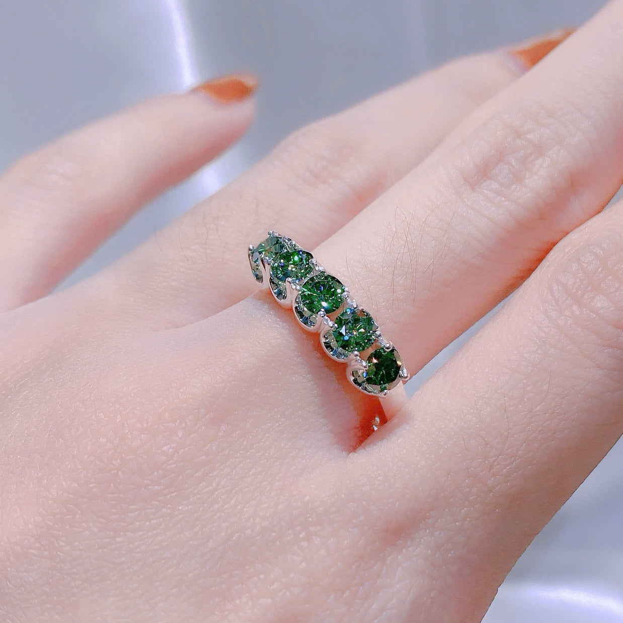Ring with green gemstones on a finger against a neutral background