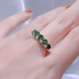Ring with green gemstones on a finger against a neutral background