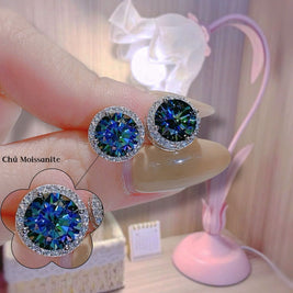 Round gemstone earrings held between fingers with a blurred background