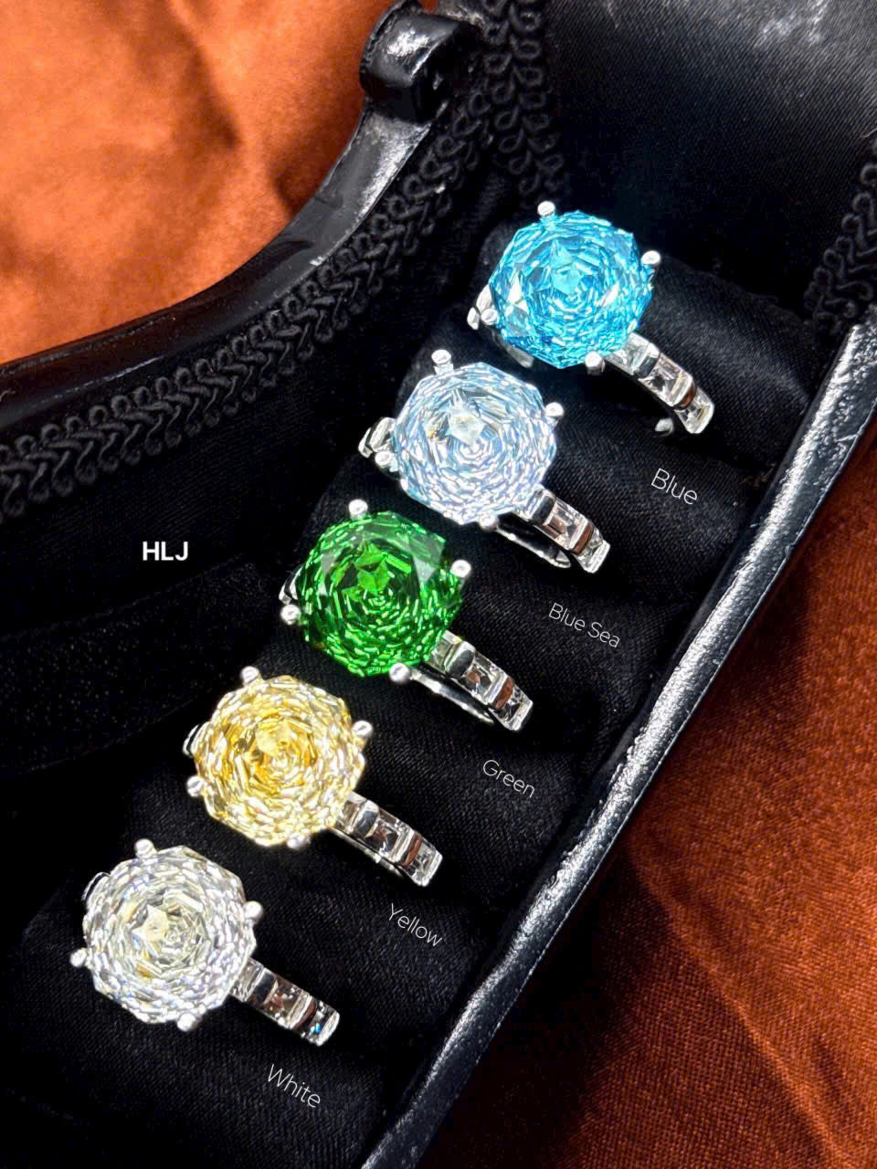 Set of colorful gemstone rings displayed on a black stand with color labels.