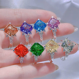 Set of colorful gemstone rings held by a hand against a neutral background