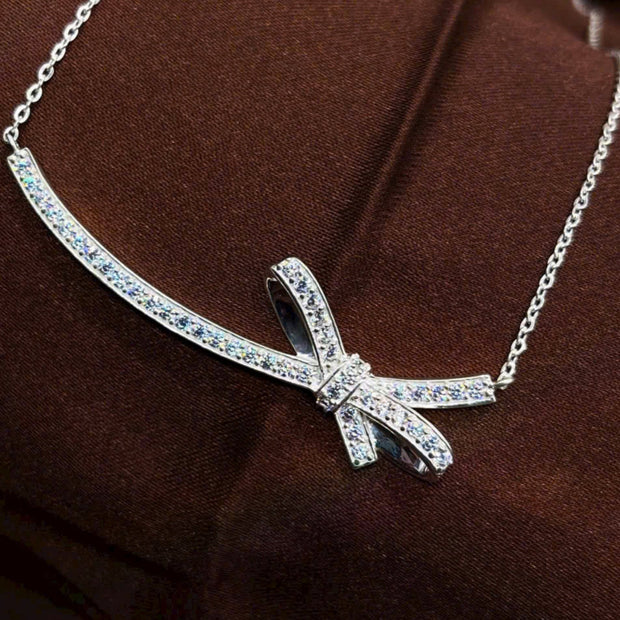 Silver bow-shaped necklace on a brown fabric background