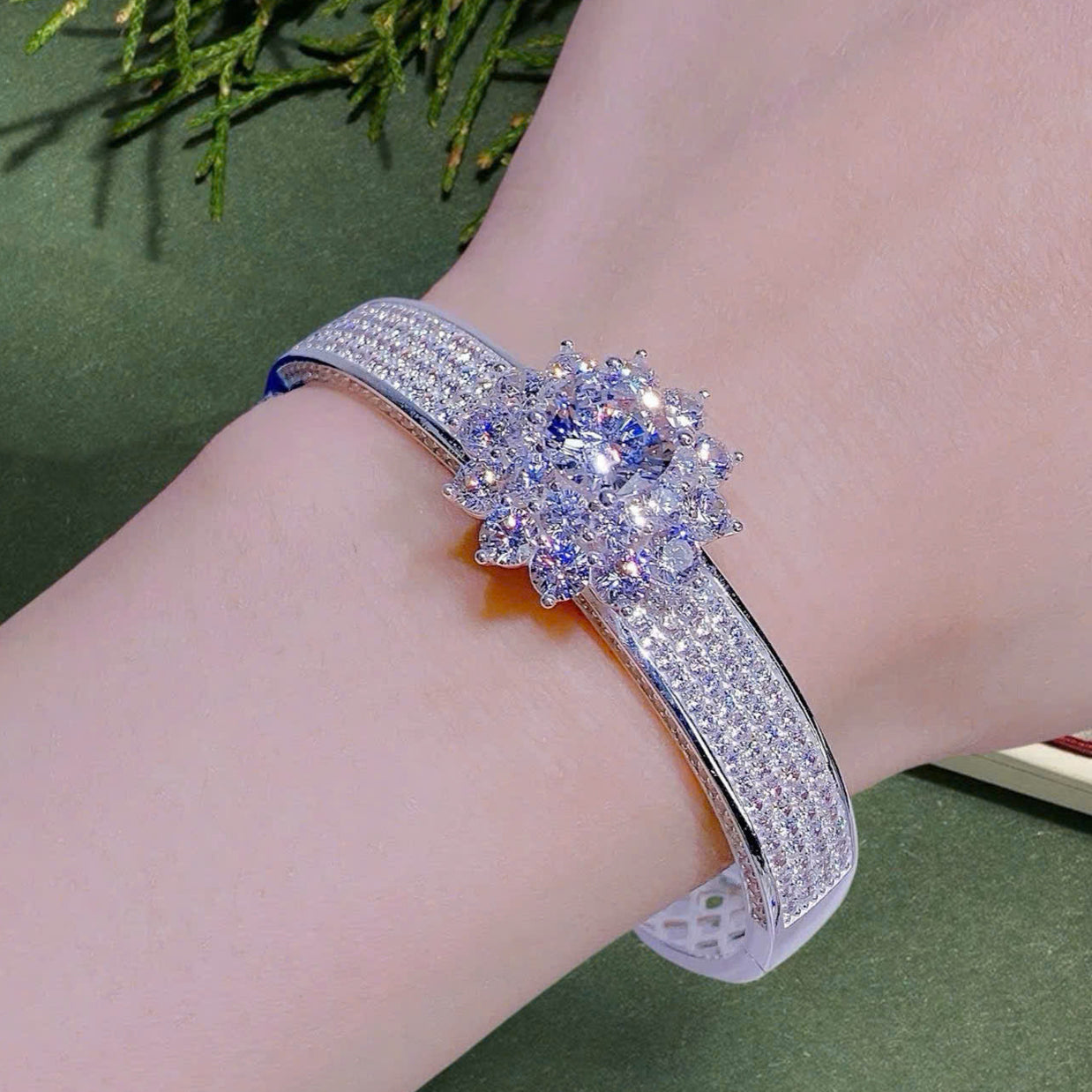 Silver bracelet with a floral design on a wrist against a ghen background