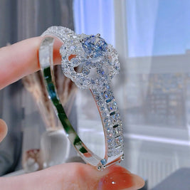 Silver bracelet with blue gemstone held by a hand against a blurred indoor background