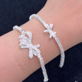 Silver bracelet with bow design on a wrist against a dark background