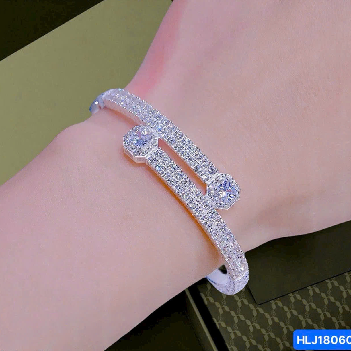 Silver bracelet with clear stones on a wrist against a green background