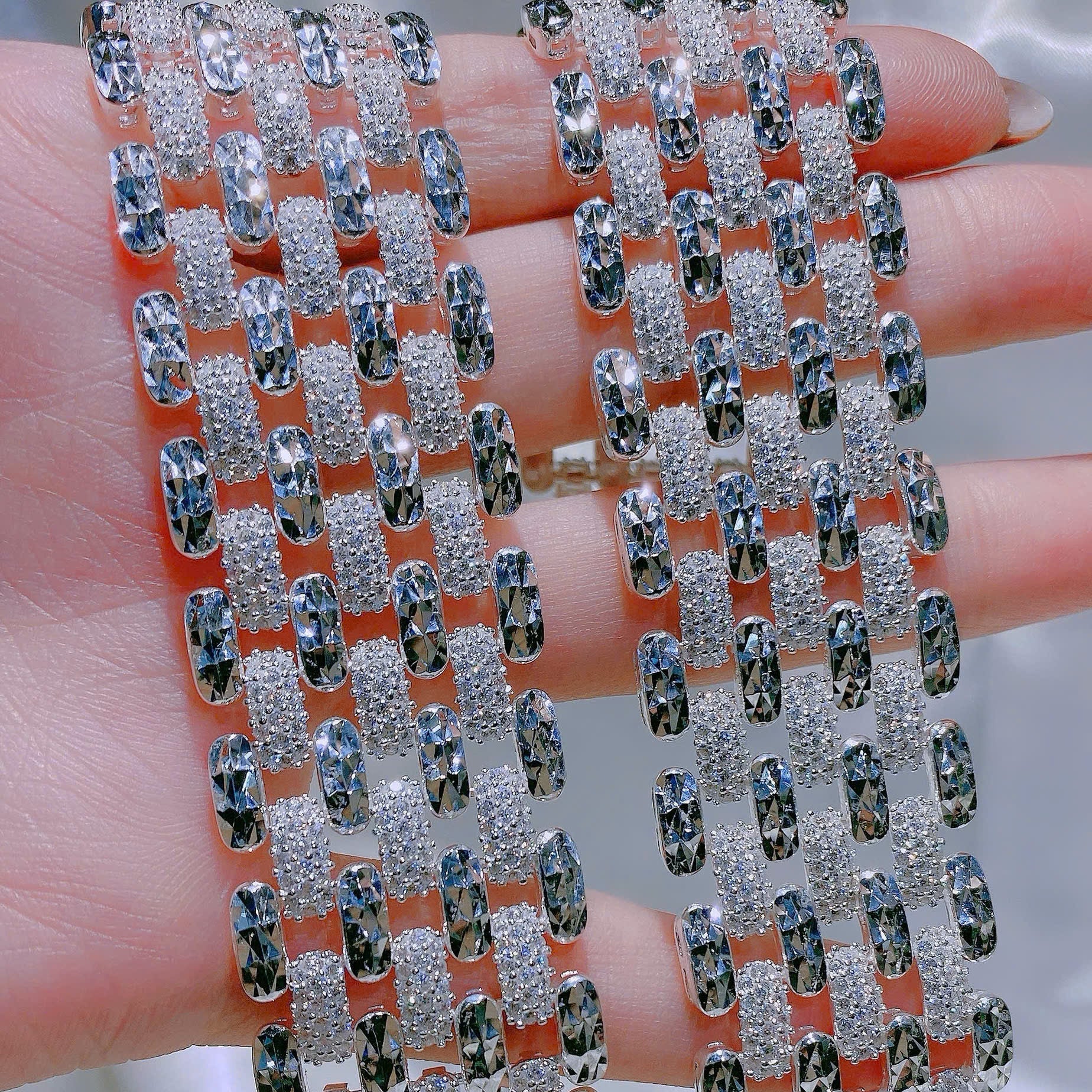 Silver bracelet with clear stones held between fingers against a neutral background