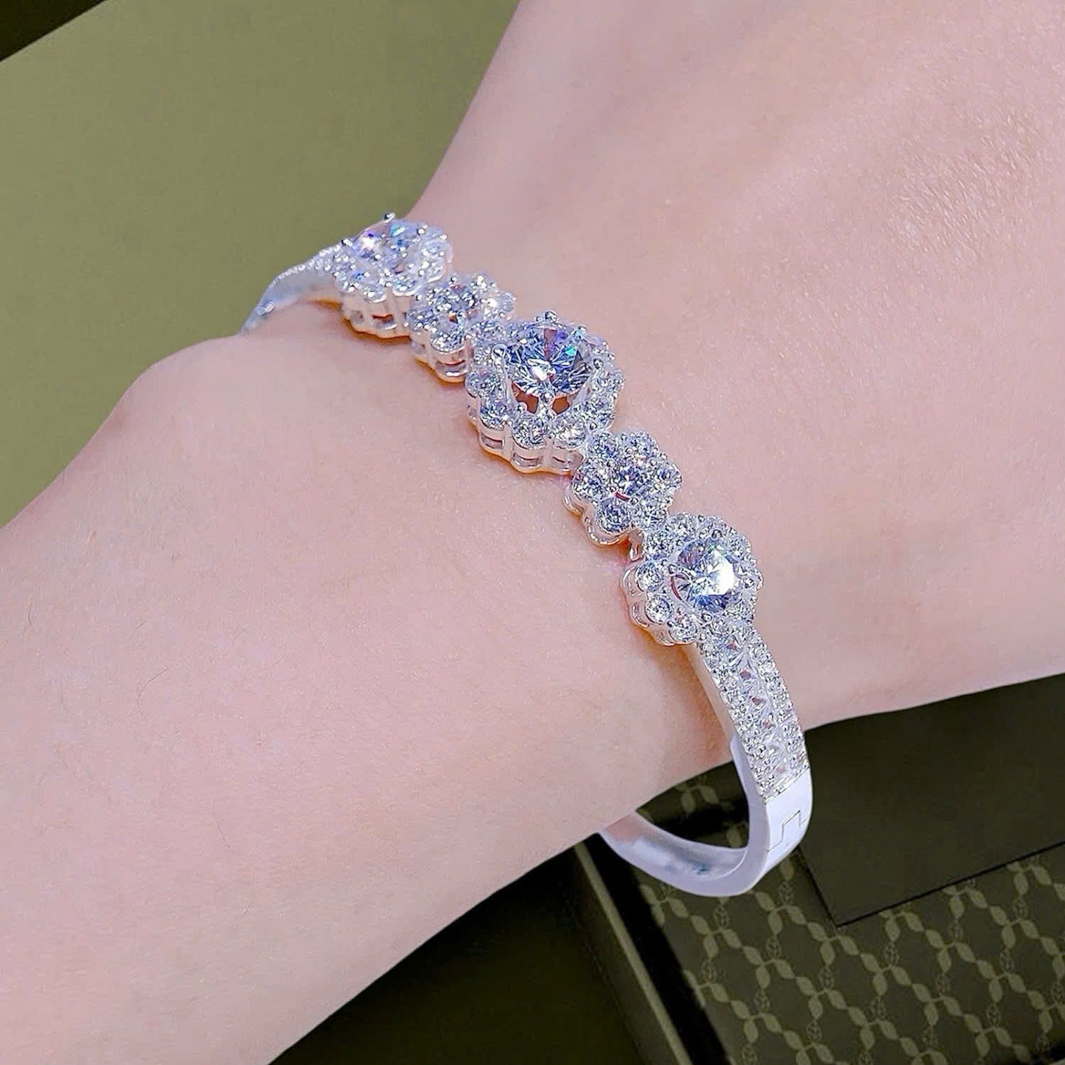Silver bracelet with clear stones on a wrist, against a green background