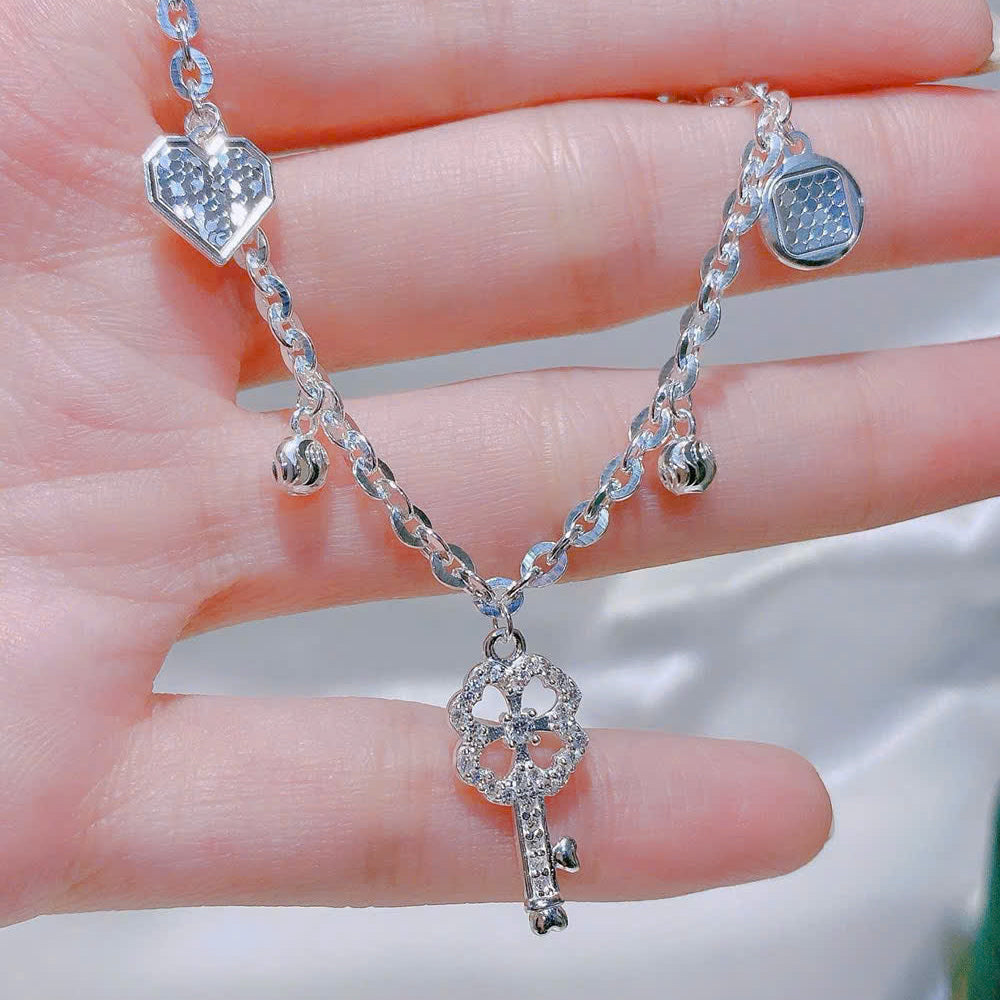 Silver bracelet with heart and key pendants on a hand against a neutral background