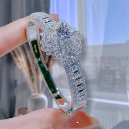 Silver bracelet with intricate design held by a hand against a blurred indoor background