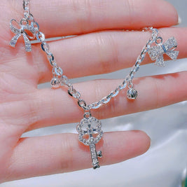 Silver bracelet with key charm held in a hand against a neutral background