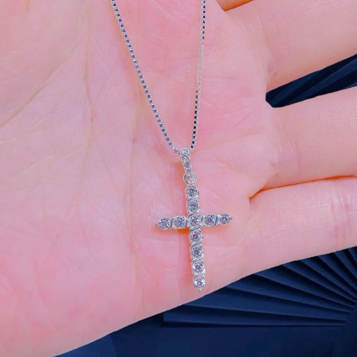 Silver cross necklace held on a hand with a blurred background