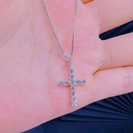 Silver cross necklace held on a hand with a blurred background