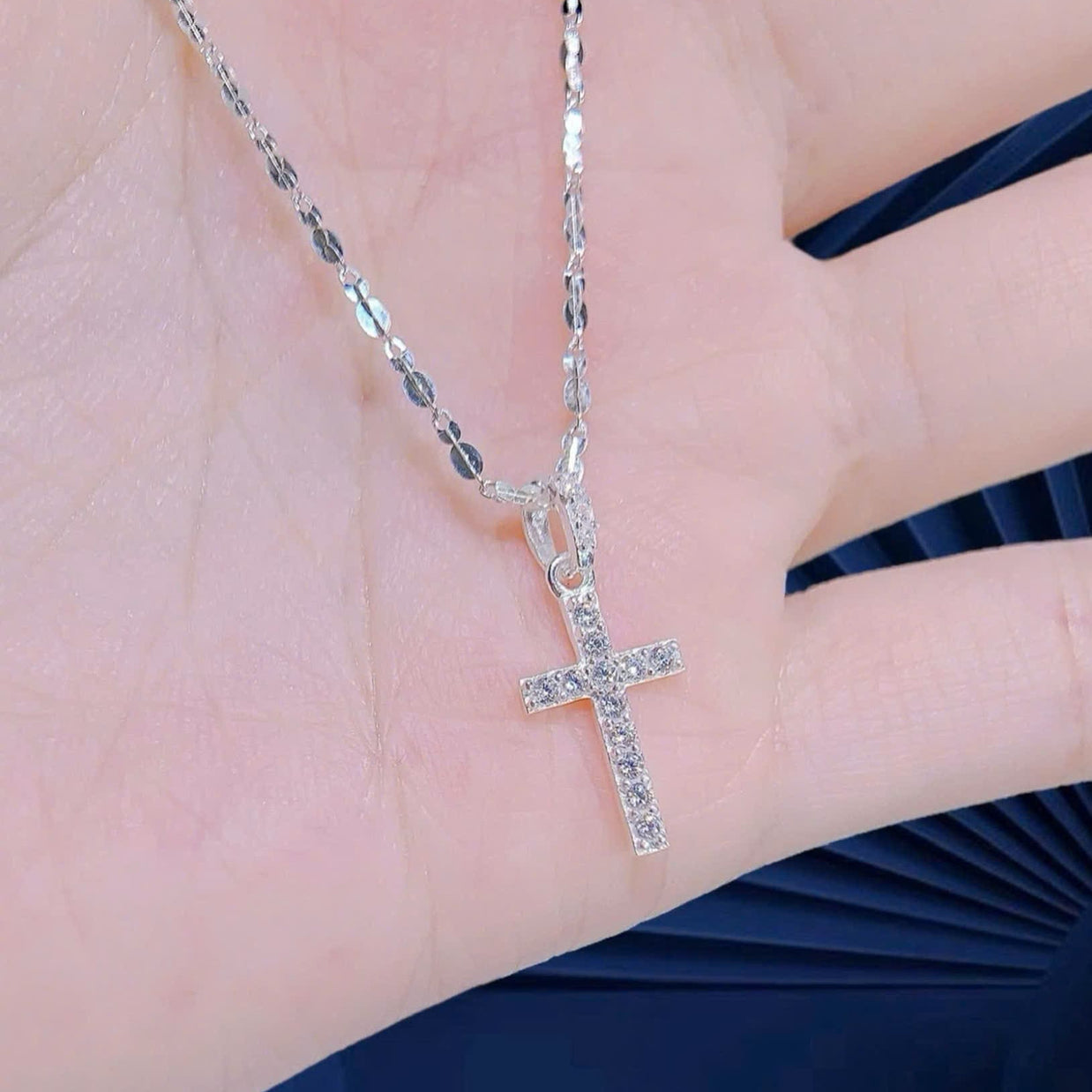 Silver cross necklace on a hand with a blue fabric background