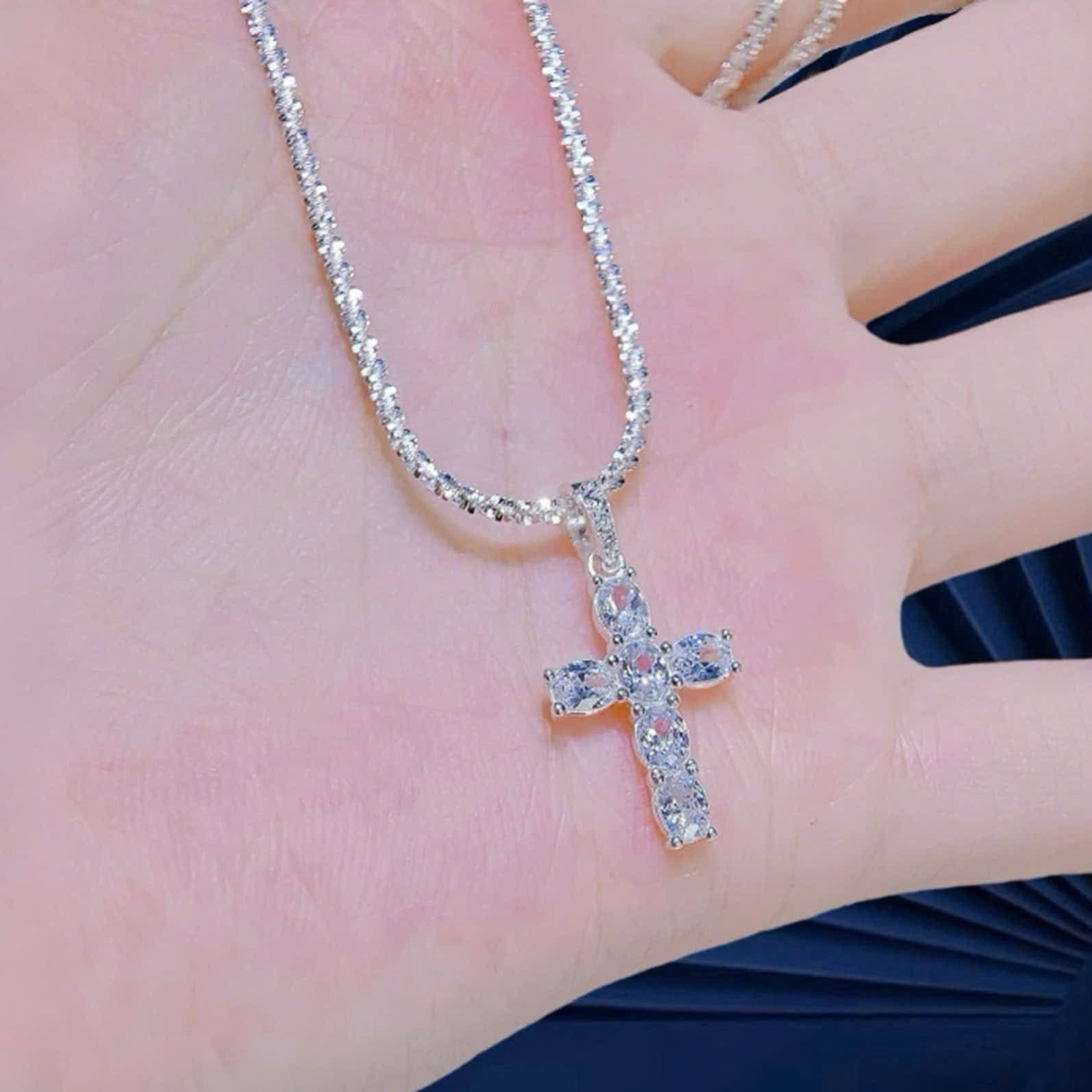 Silver cross necklace on a hand with a blurred background