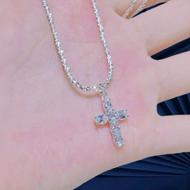 Silver cross necklace on a hand with a blurred background