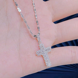 Silver cross necklace on a hand with a blurred background