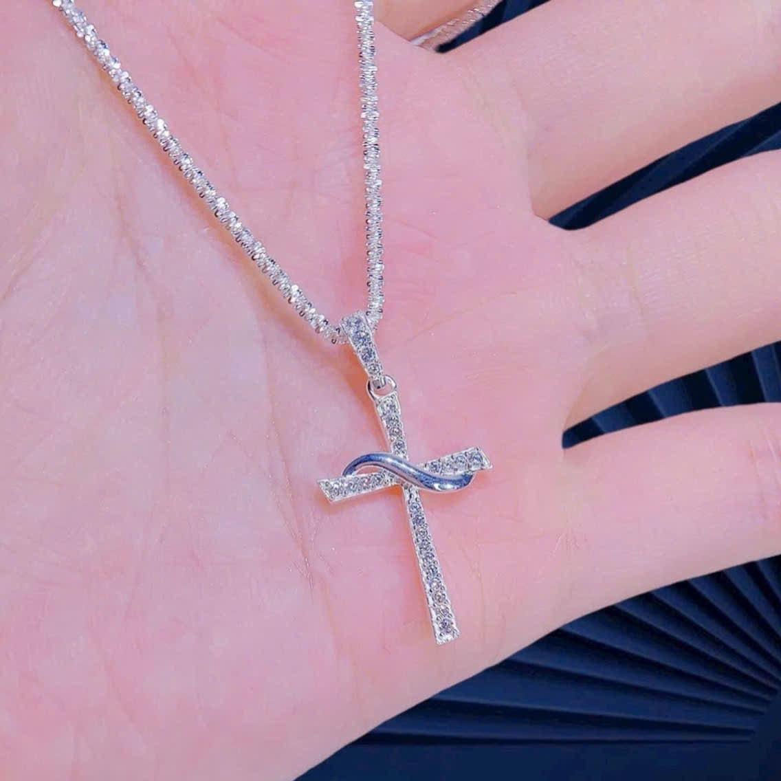 Silver cross necklace with diamonds on a hand