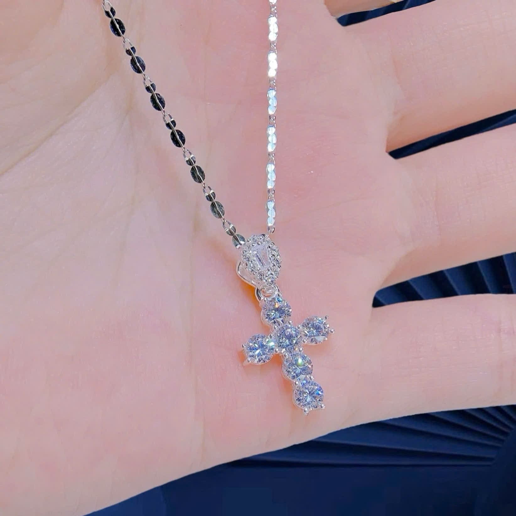 Silver cross necklace with gemstones on a hand against a blue background