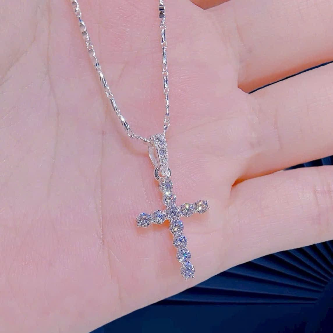 Silver cross necklace with small stones held in a hand against a neutral background