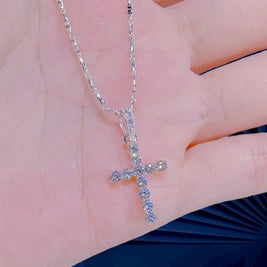 Silver cross necklace with small stones held in a hand against a neutral background