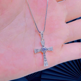 Silver cross pendant on a hand with a blurred background