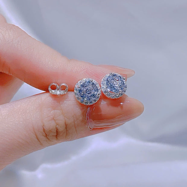 Silver earrings held between fingers against a neutral background