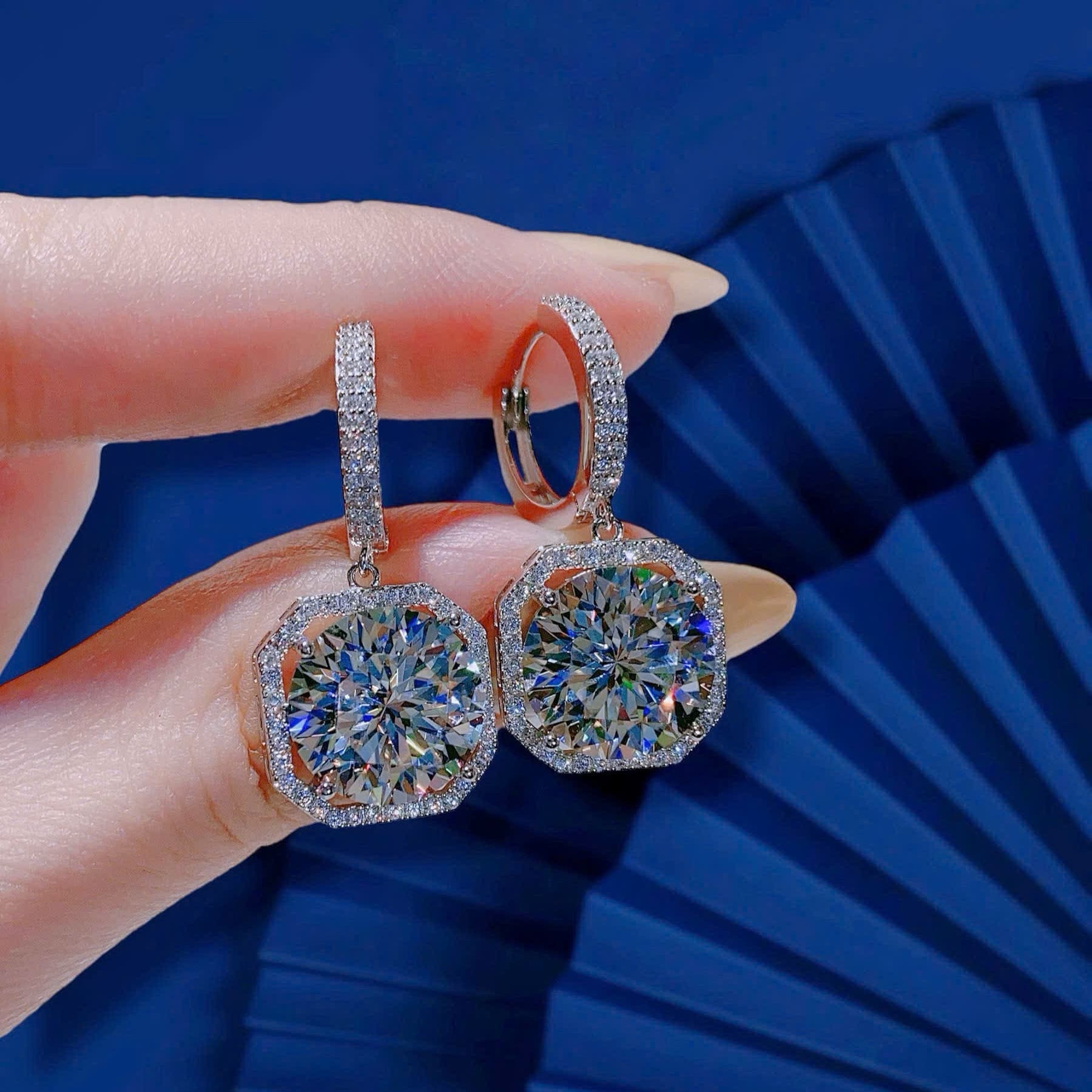 Silver earrings held by a hand against a blue background