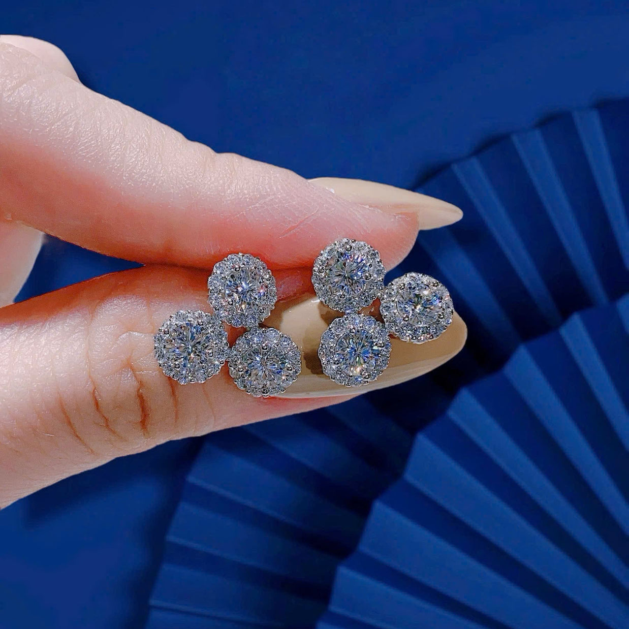 Silver earrings held by a hand against a blue background
