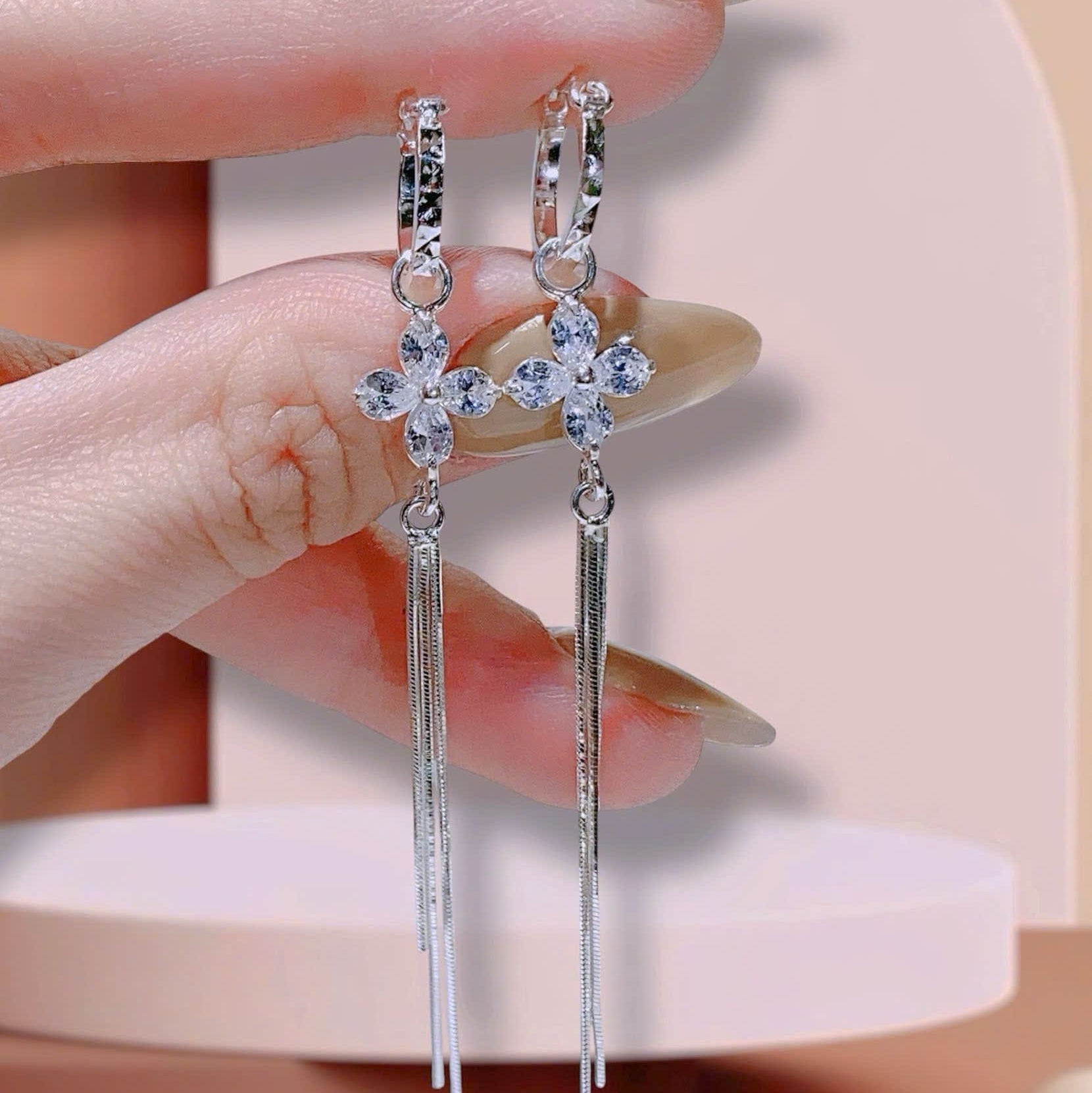 Silver earrings held by a hand against a neutral background