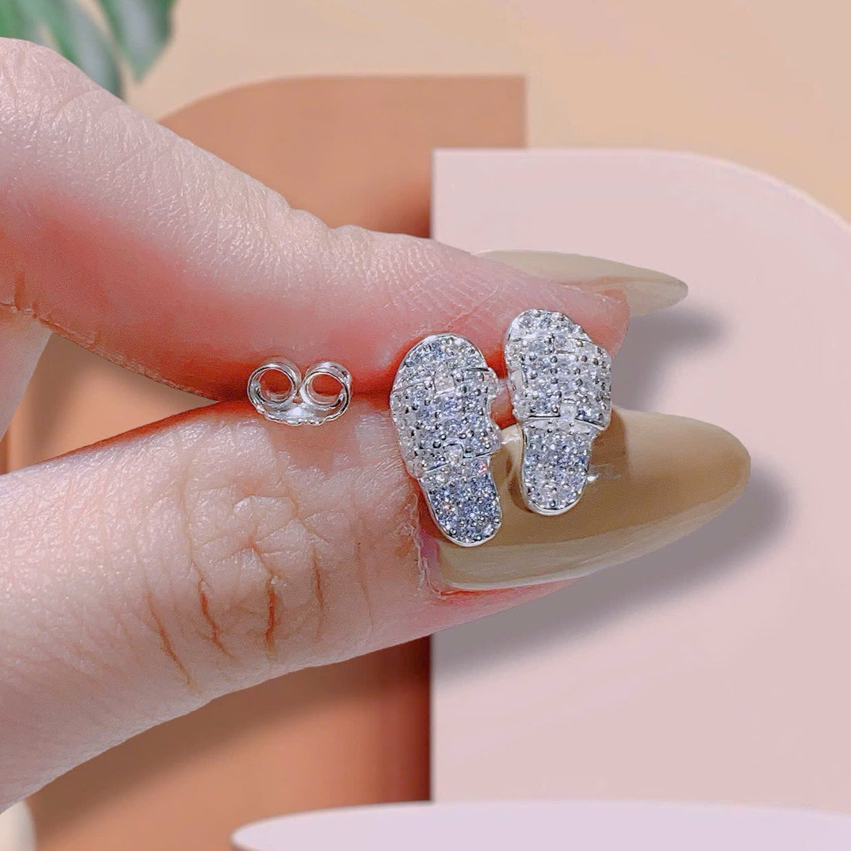 Silver earrings held by a hand with a neutral background