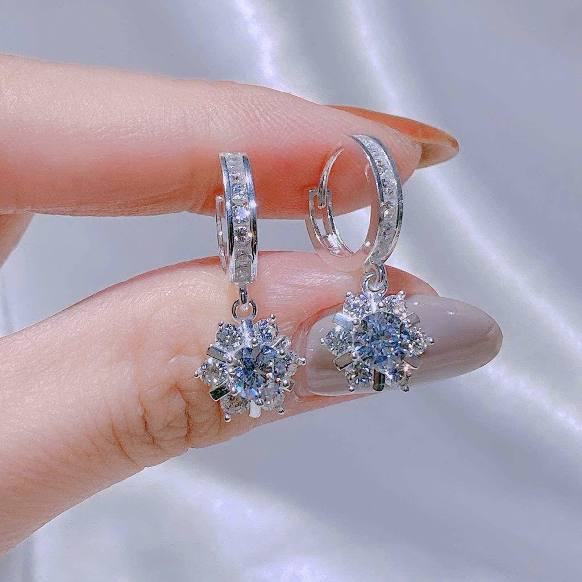 Silver earrings with gemstones held between fingers against a neutral background