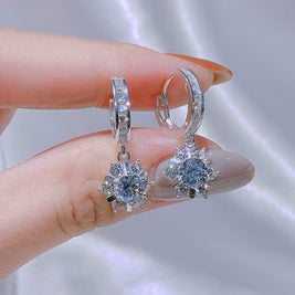Silver earrings with gemstones held between fingers against a neutral background