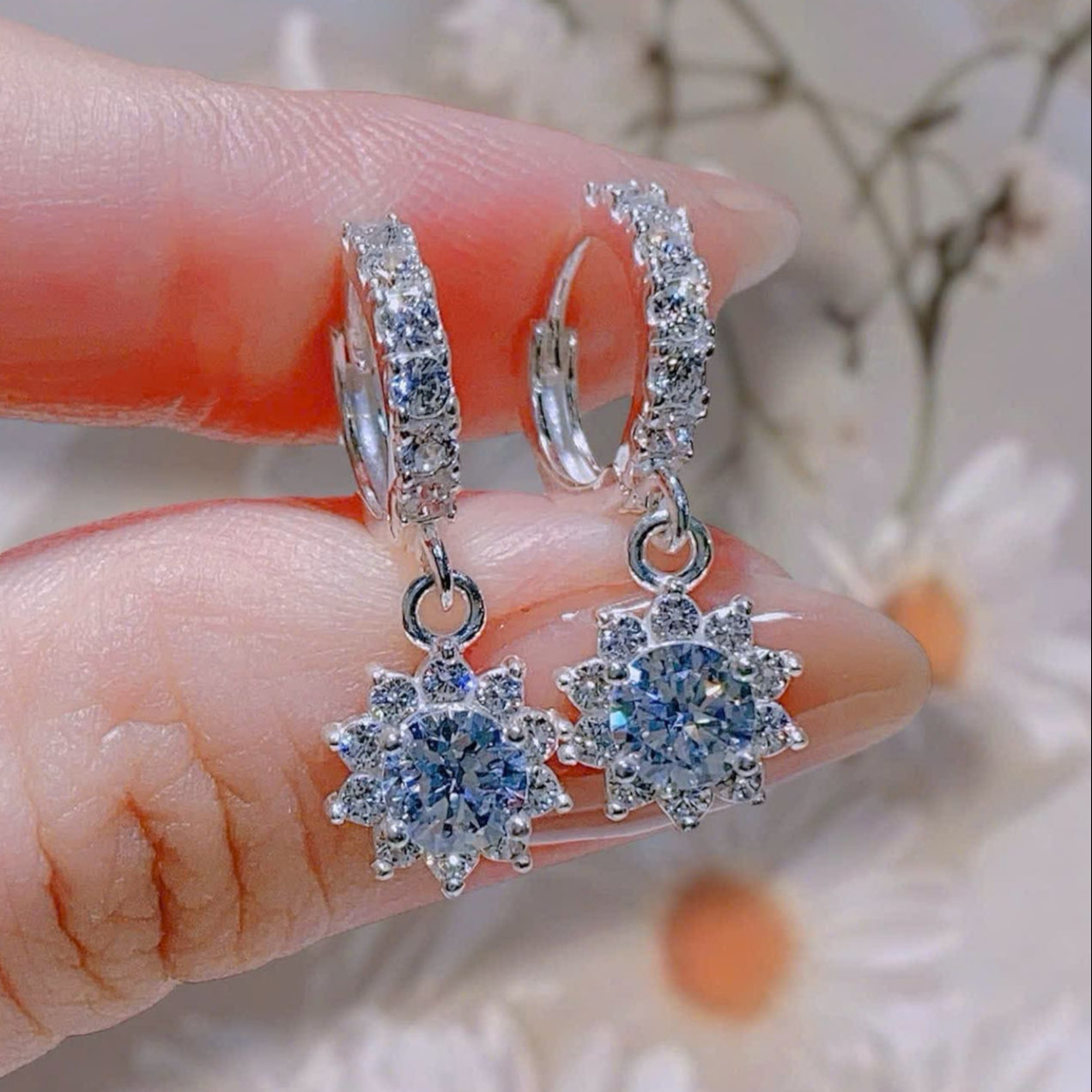 Silver earrings with blue gemstones held between fingers against a floral background