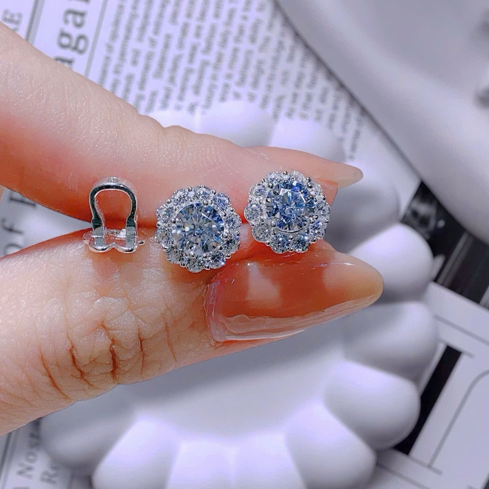 Silver earrings with blue gemstones held between fingers on a newspaper background