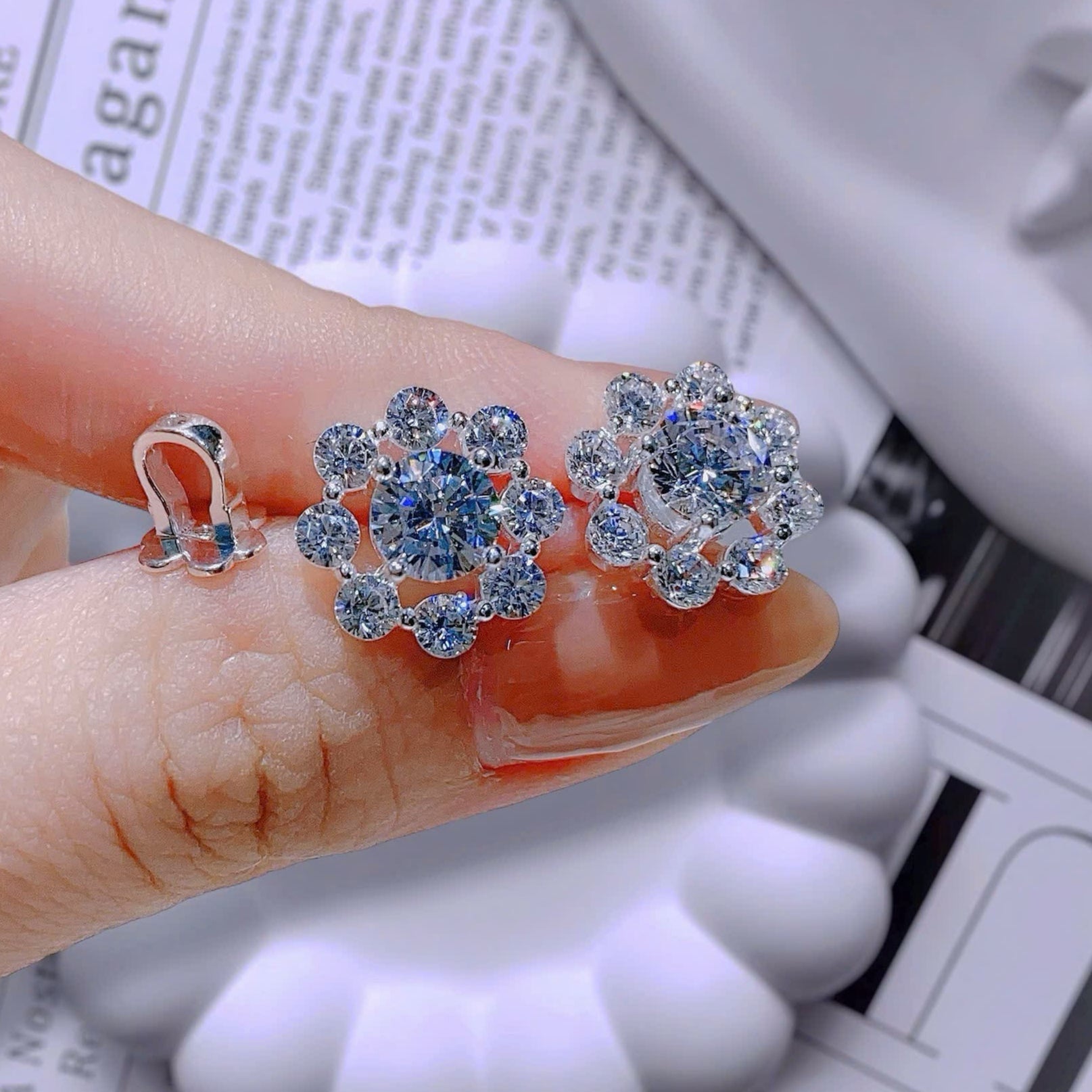 Silver earrings with blue gemstones held between fingers on a newspaper background