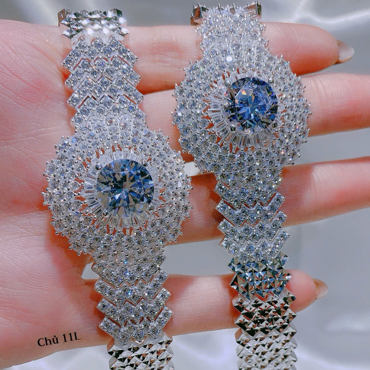 Silver earrings with blue gemstones held in hand against a neutral background