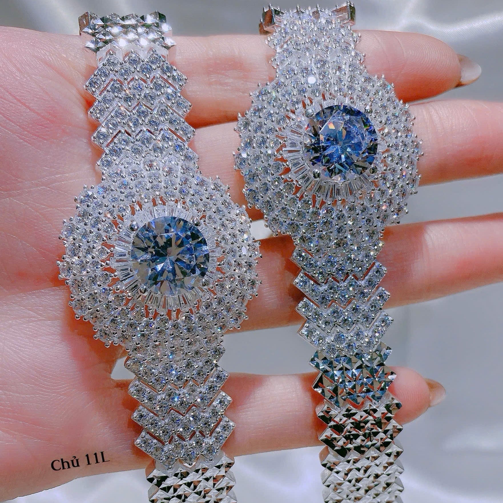 Silver earrings with blue gemstones held in hand against a neutral background