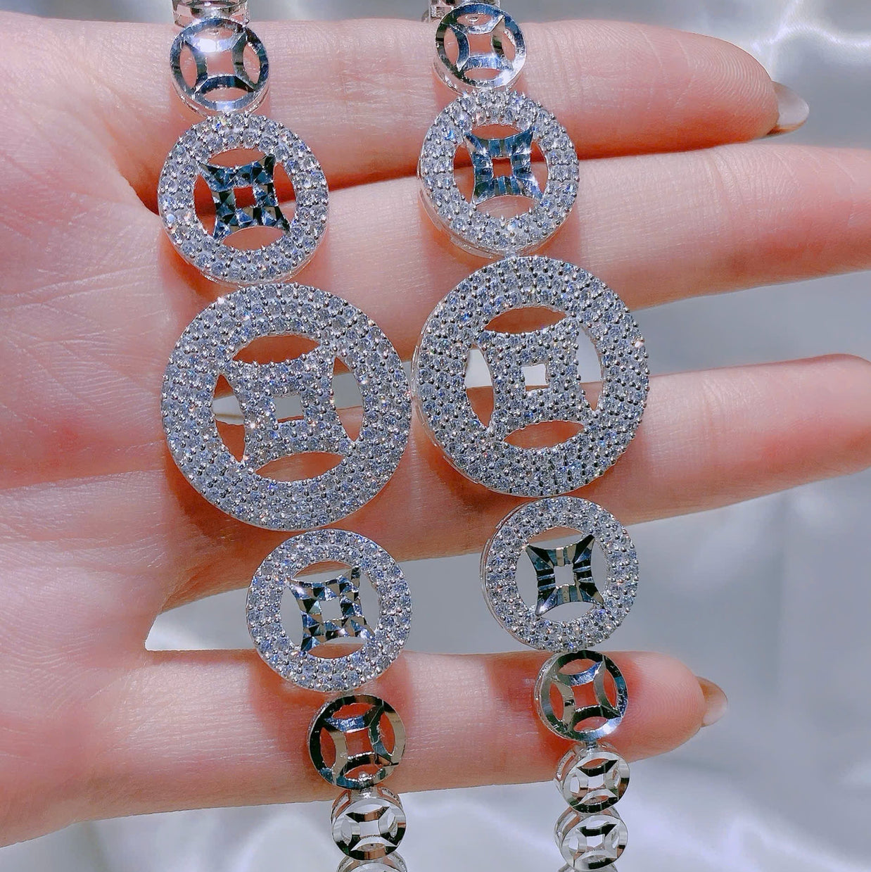 Silver earrings with circular design held by a hand against a neutral background