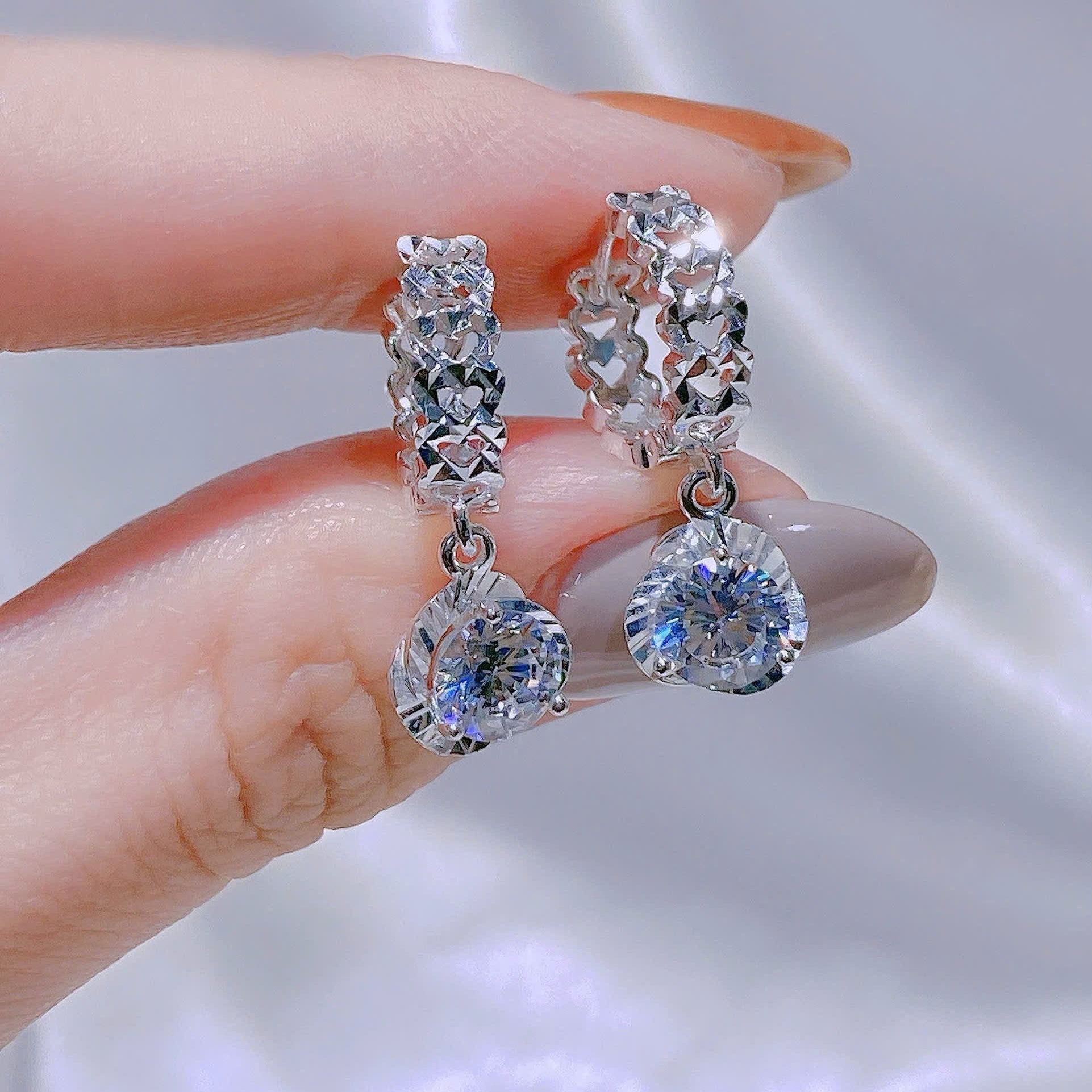 Silver earrings with clear gemstones held by a hand against a neutral background