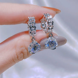 Silver earrings with clear gemstones held by a hand against a neutral background