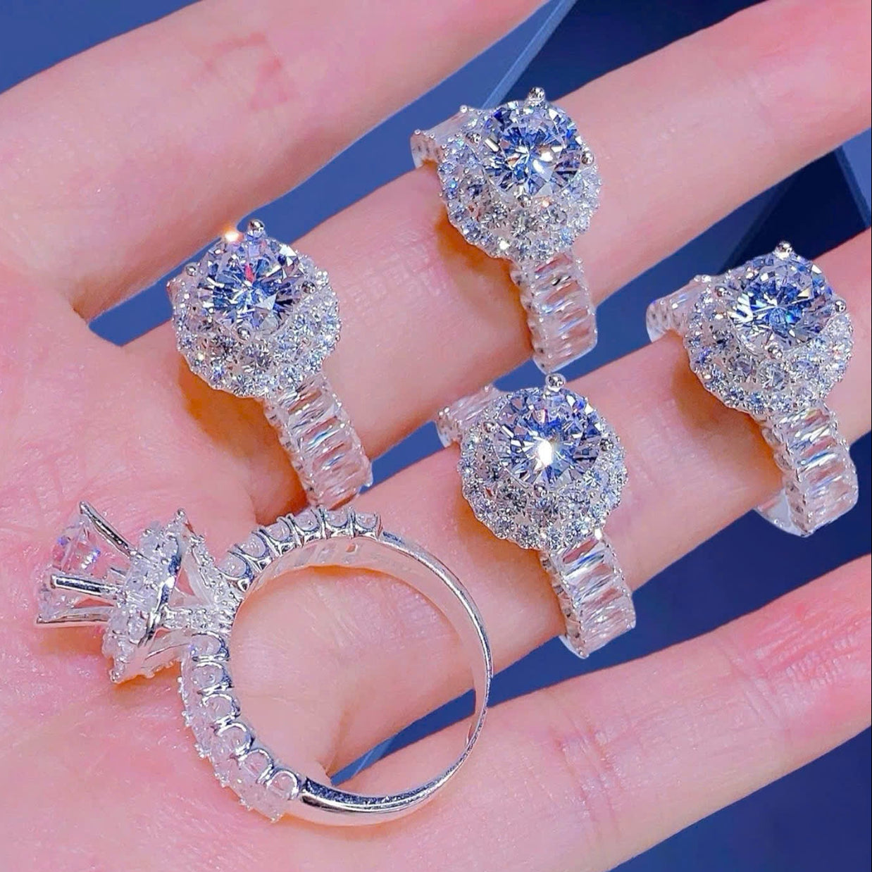 Silver earrings with clear gemstones held in a hand against a blue background