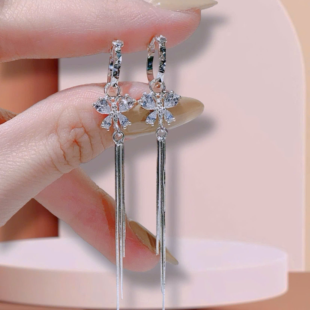 Silver earrings with dangling elements held by a hand against a neutral background