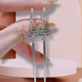 Silver earrings with dangling elements held by a hand against a neutral background