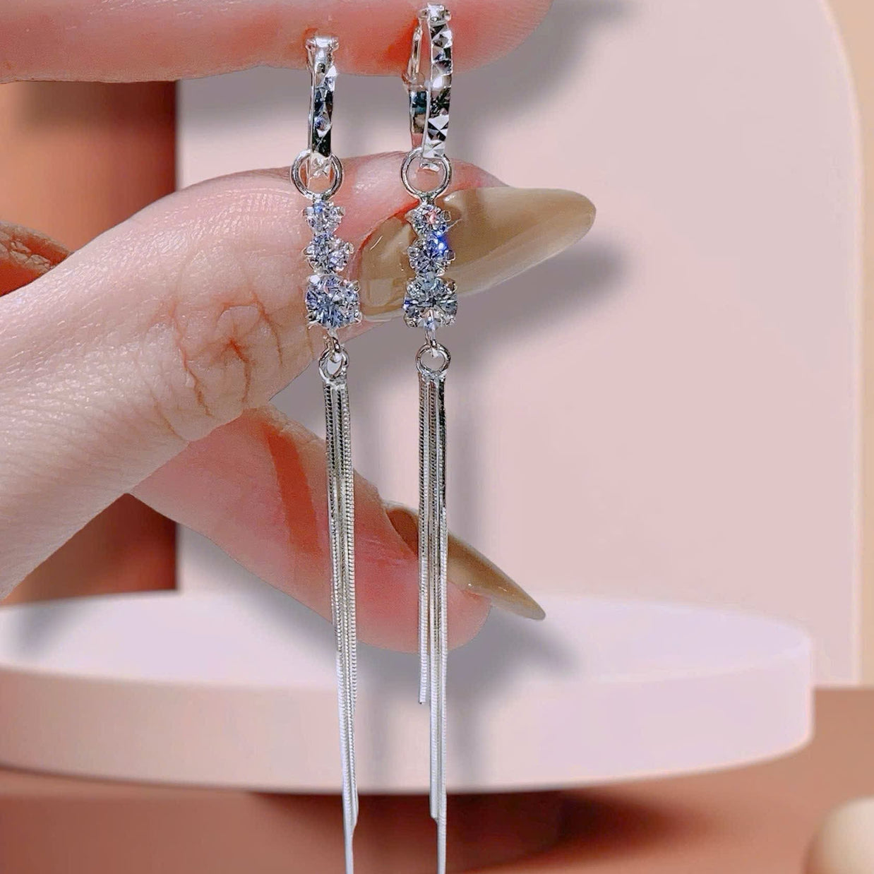 Silver earrings with dangling elements held by a hand against a neutral background
