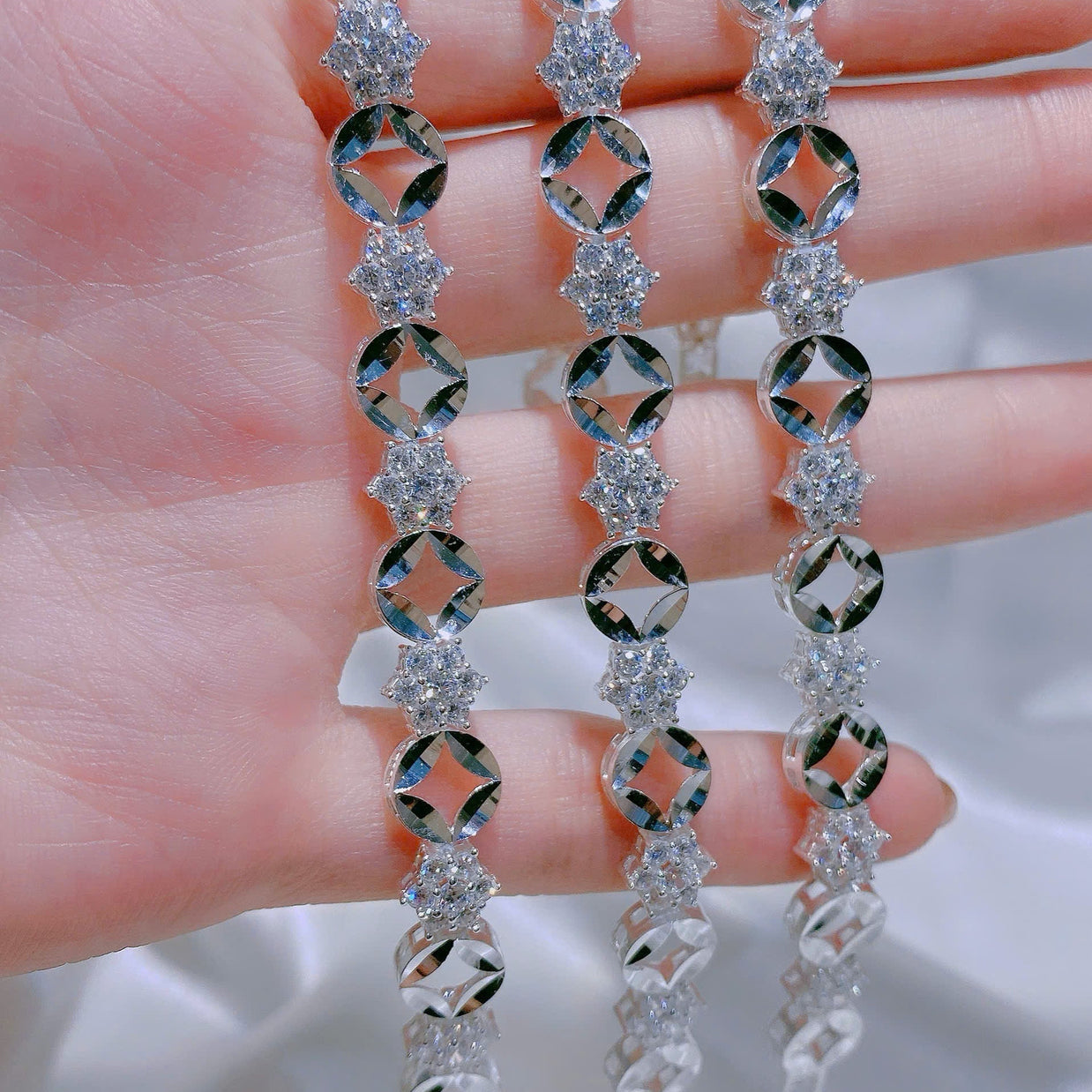 Silver earrings with diamond-like stones held between fingers against a neutral background