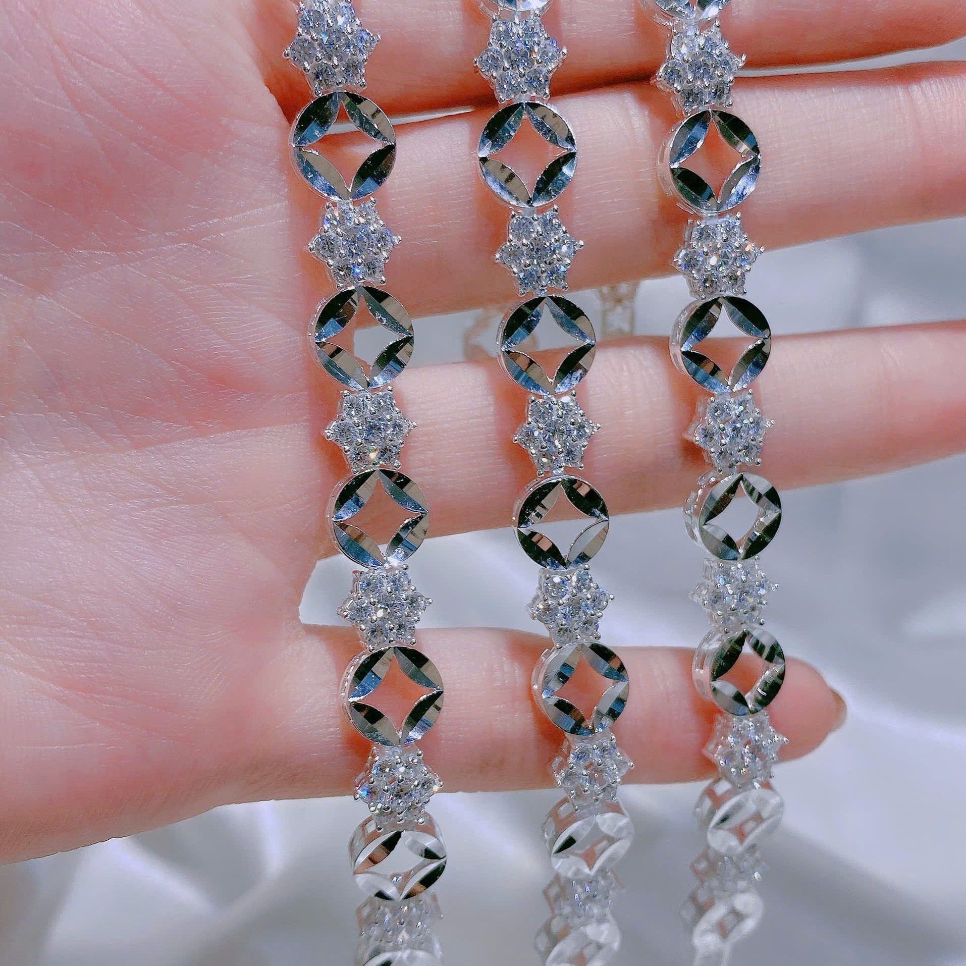 Silver earrings with diamond-like stones held between fingers against a neutral background