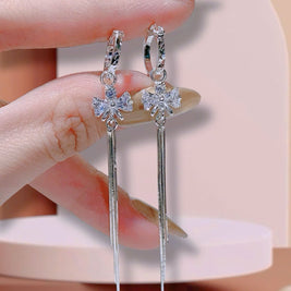 Silver earrings with floral and teardrop designs held by a hand against a neutral background.