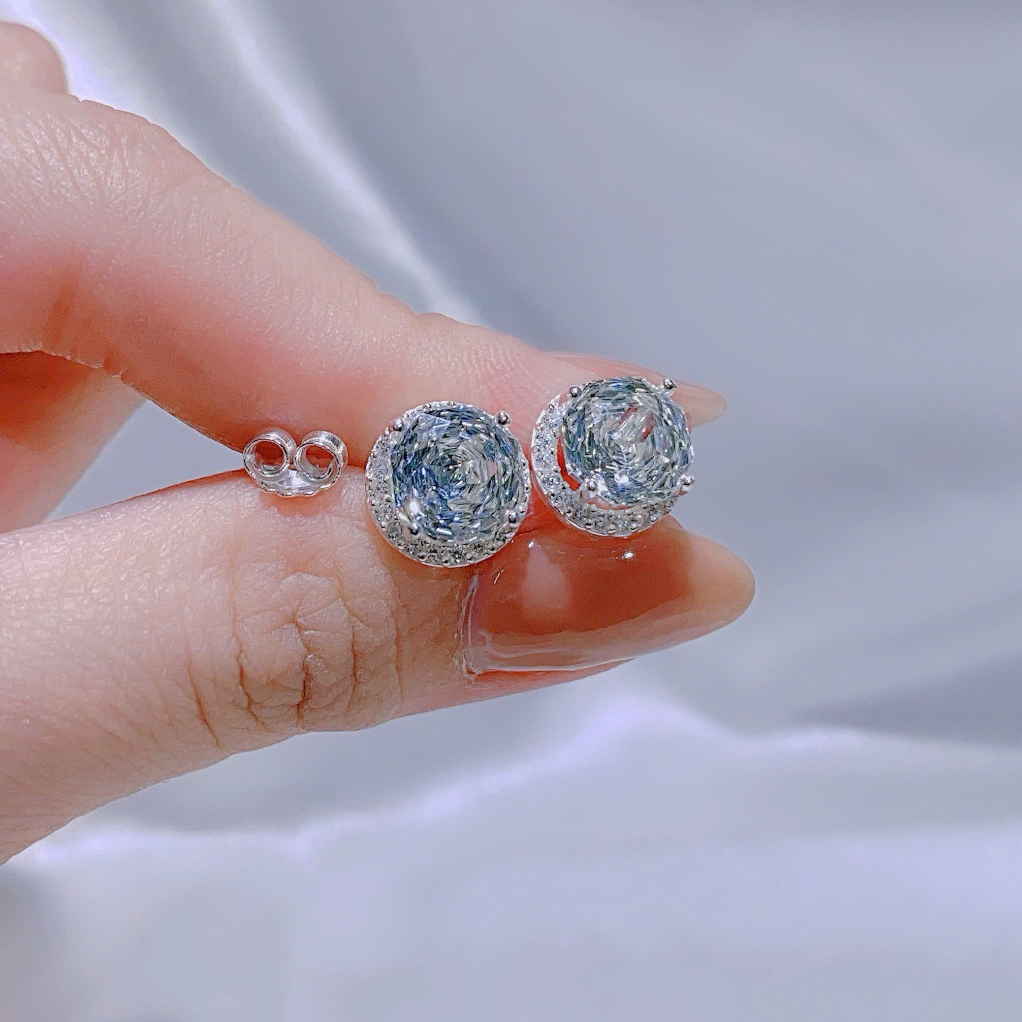 Silver earrings with gemstones held between fingers against a light background