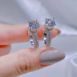 Silver earrings with gemstones held between fingers against a neutral background
